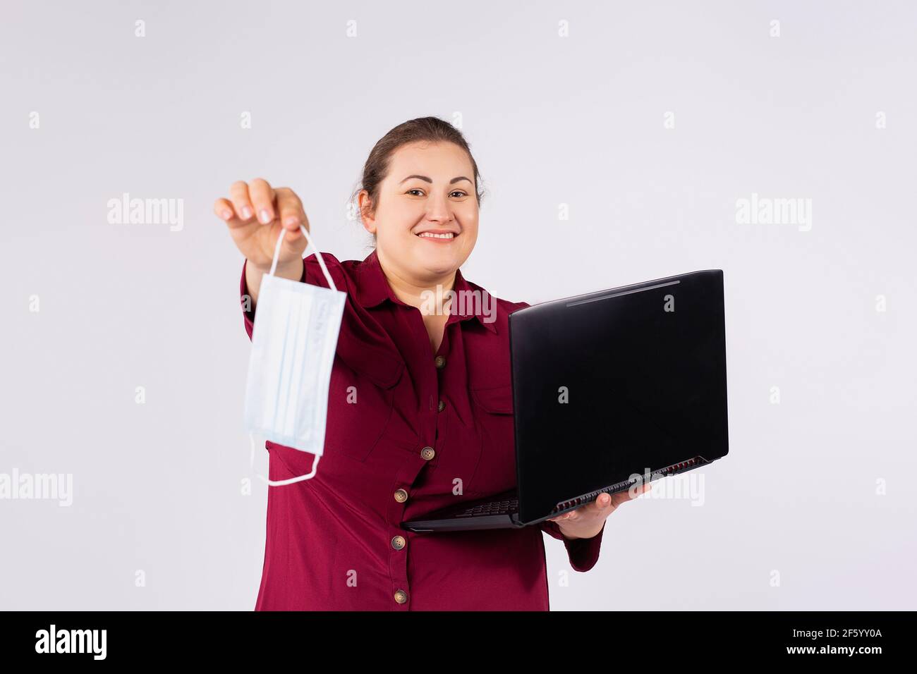 Geschäftsfrau geschützt hält Laptop-Computer zeigt eine Einweg-OP-Gesichtsmaske. Betrieb eines Unternehmens während einer gefährlichen Virus- oder Bakterienepidemie Stockfoto