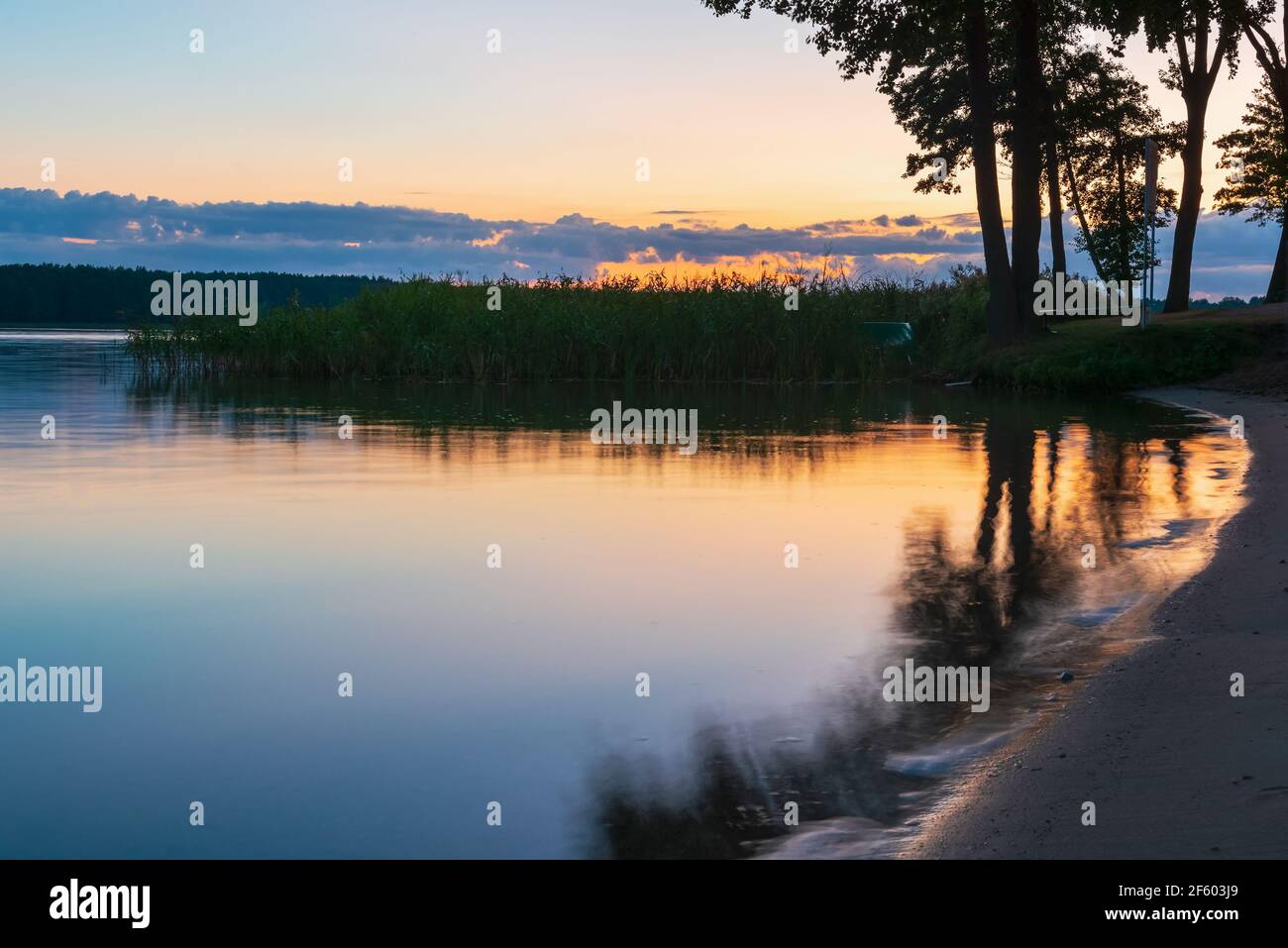 Ruhiger See und Sandstrand mit Bäumen und dunkelblauem Himmel, ruhige Naturlandschaft bei Nacht Stockfoto