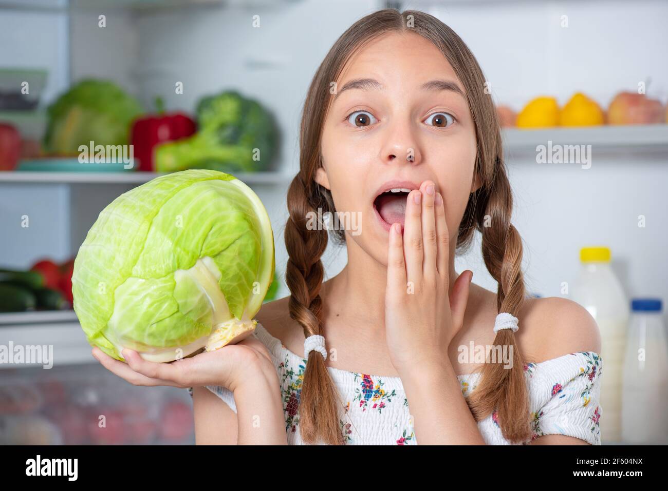 Schöne junge Teenager-Mädchen hält frischen grünen Kohl im Stehen In der Nähe offenen Kühlschrank in der Küche zu Hause Stockfoto