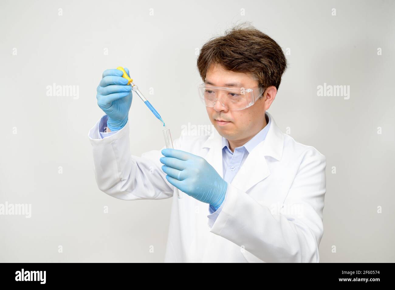 Porträt eines asiatischen Wissenschaftlers mit einem weißen Laborkleid und Handschuhen, der einen experimentellen Behälter in der Hand hält. Stockfoto