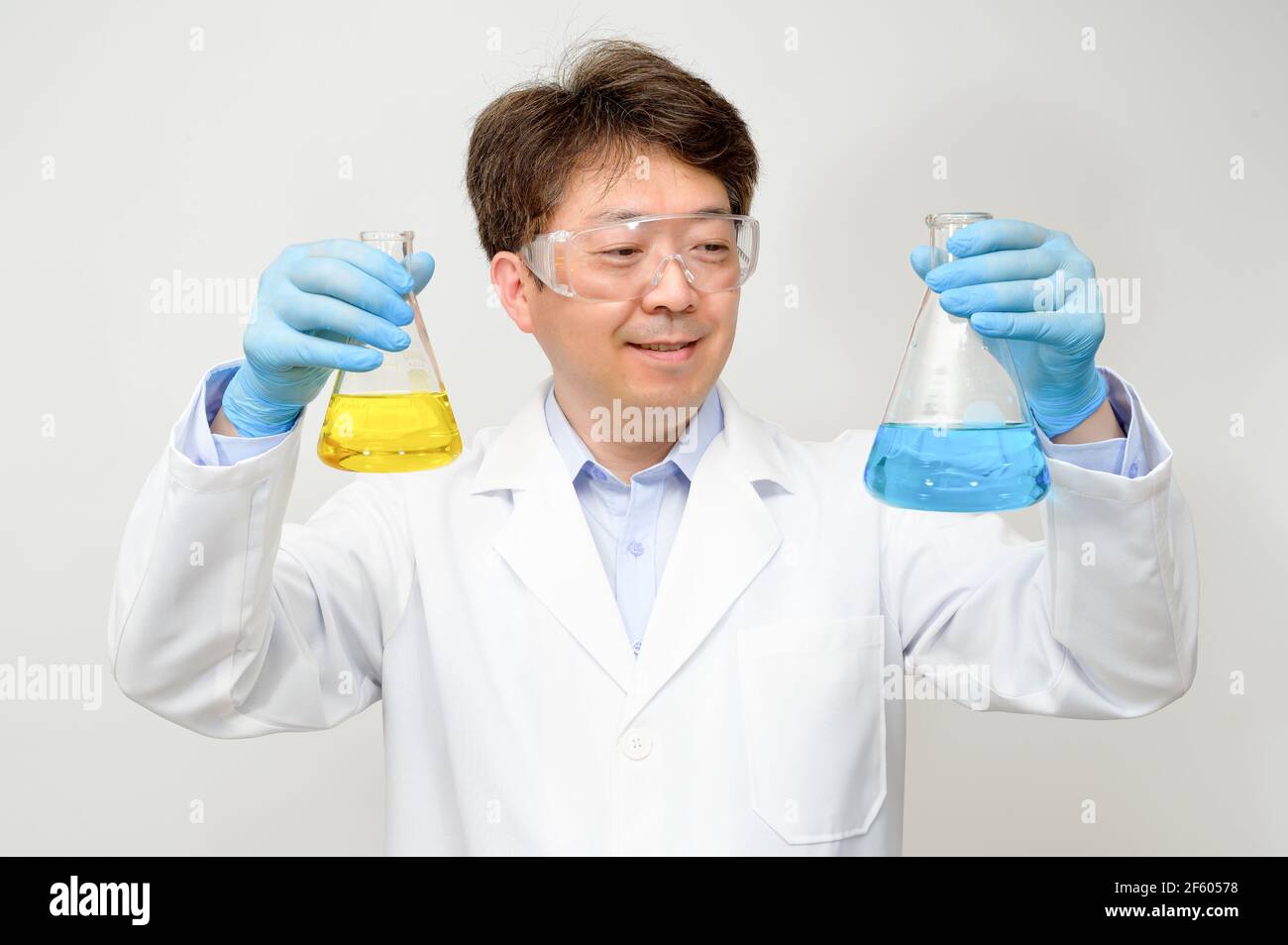 Porträt eines asiatischen Wissenschaftlers mit einem weißen Laborkleid und Handschuhen, der einen experimentellen Behälter in der Hand hält. Stockfoto