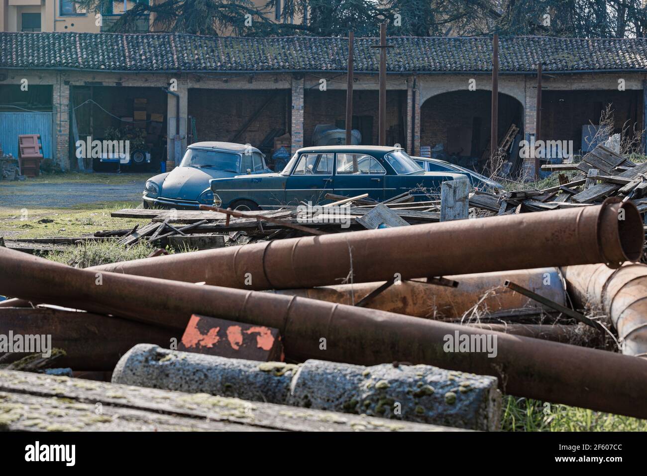 Große Rosty Pfeifen und alte Rosty Autos verlassen in einem Feld und zerbröckelt Lager im Hintergrund. Stockfoto