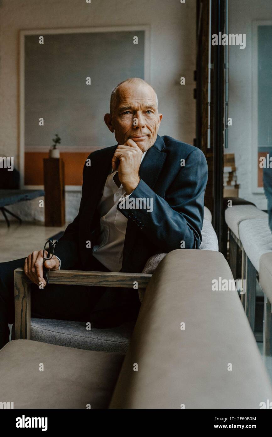 Porträt eines männlichen Unternehmers mit der Hand auf dem Kinn, über dem er sitzt Sofa im Büro Stockfoto