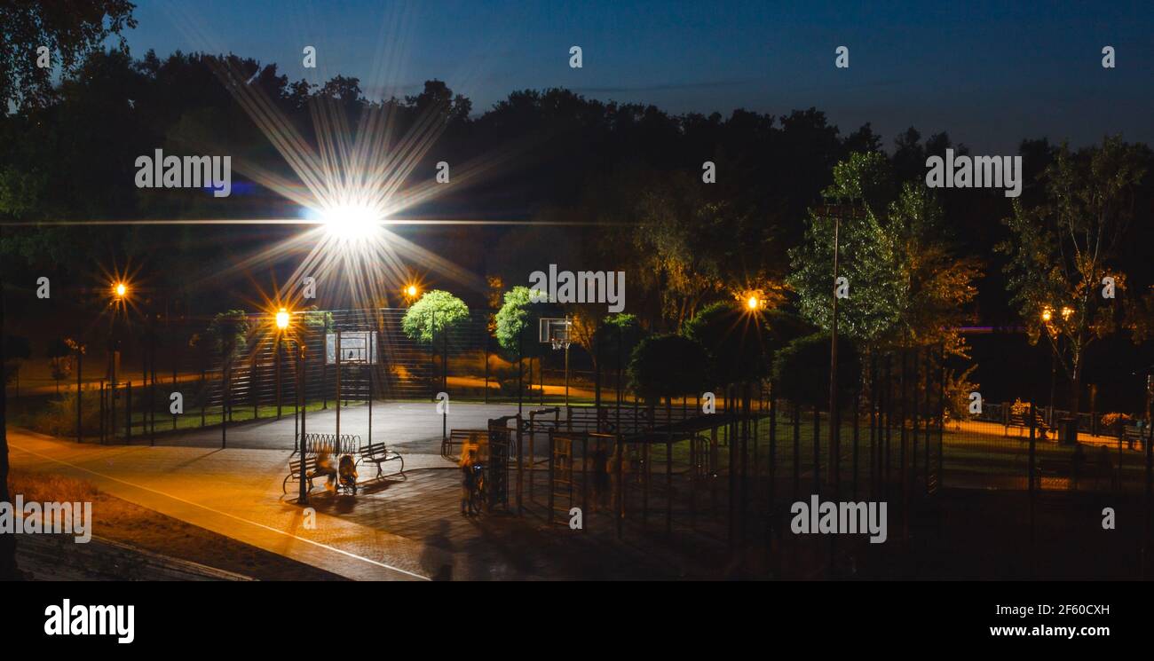 Grüne Nacht leerer Spielplatz im Park mit hellem Scheinwerfer auf blauem Hintergrund. Abend Stadt Stadtlandschaft. Niemand im Sommer öffentlichen Platz. Sport Stockfoto