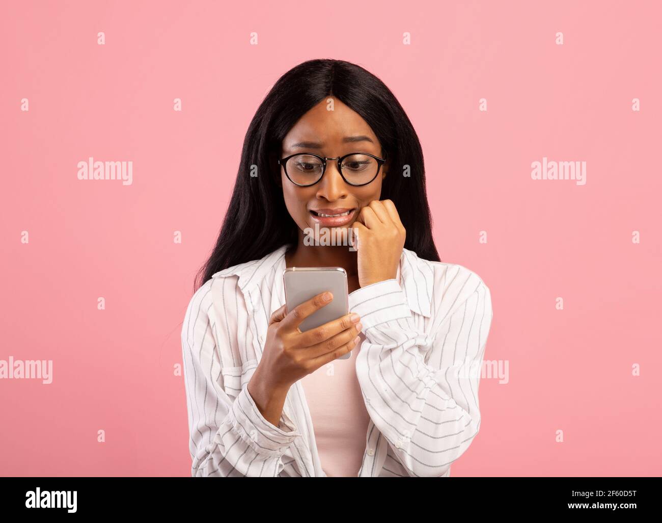 Hoppla. Peinlich schwarze Frau Blick auf Handy-Bildschirm in Verwirrung auf rosa Studio Hintergrund Stockfoto