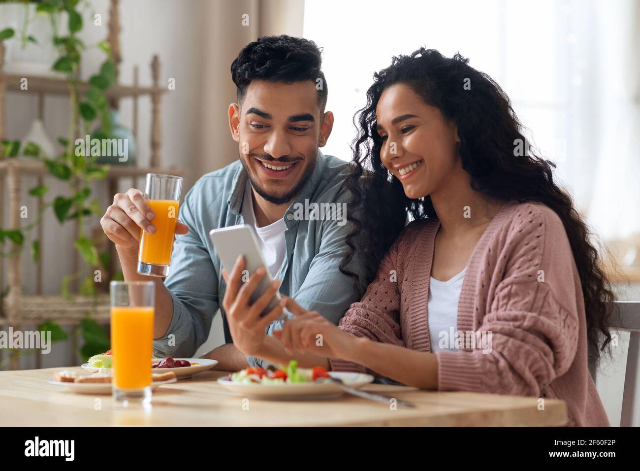 Nahöstliches Paar, das beim Frühstück Fotos auf dem Smartphone ansieht In der Küche Stockfoto