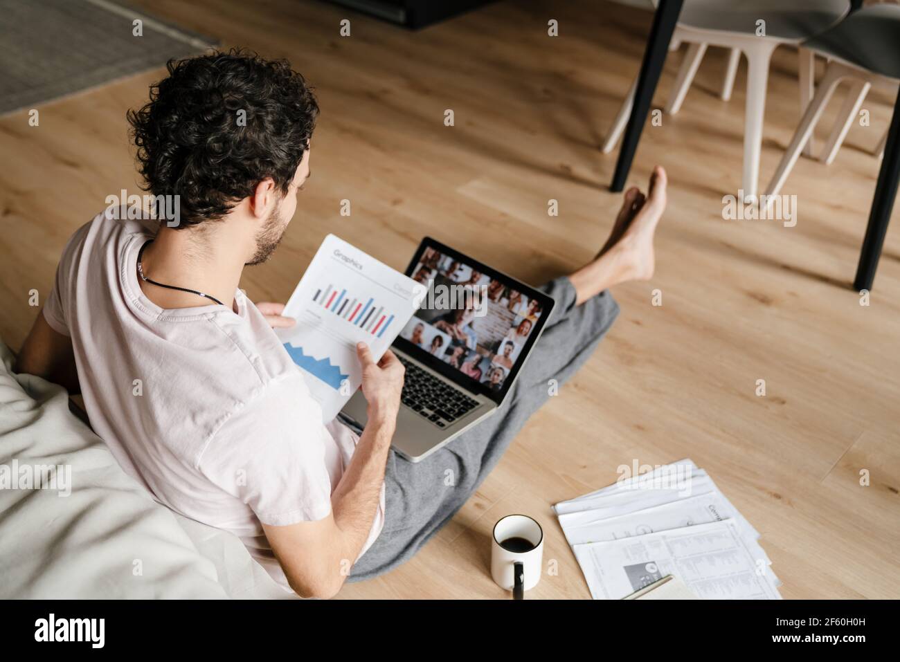 Fokussierter Mann, der mit Papieren arbeitet und Konferenzanruf macht Laptop, während Sie zu Hause auf dem Boden sitzen Stockfoto
