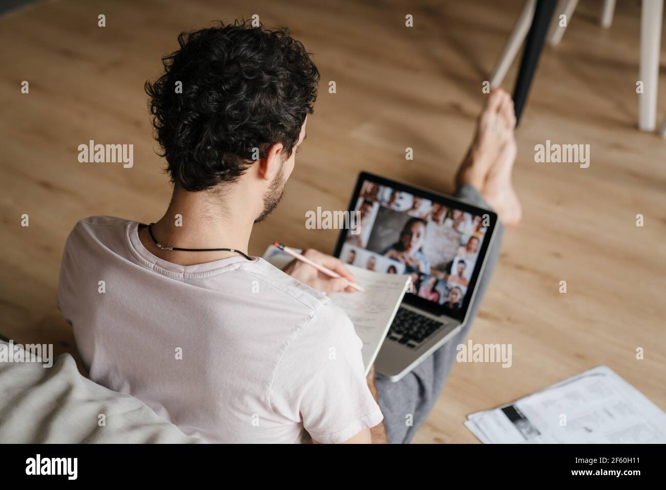 Fokussierter Mann, der mit Papieren arbeitet und Konferenzanruf macht Laptop, während Sie zu Hause auf dem Boden sitzen Stockfoto