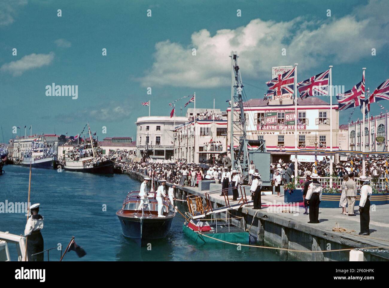 Crowd Scenes in Bridgetown, Barbados, 1955, während der Karibik-Tour von Prinzessin Margaret. Hier säumen Menschenmassen den Hafen am Trafalgar Square (heute National Heroes Square genannt). Hier kommt ein Tender der vertäuten Royal Yacht ‘Britannia’. Im Januar 1955 unternahm die Prinzessin ihre ersten Reisen in die Karibik, ihre Reise an Bord von Britannia in die britischen Kolonien war in ganz Westindien beliebt. Prinzessin Margaret (1930 – 2002) war die Schwester von Königin Elisabeth II. Dieses Bild stammt von einem alten Amateur-35-mm-Farbtransparenz – einem Vintage-Foto aus den 1950er Jahren. Stockfoto