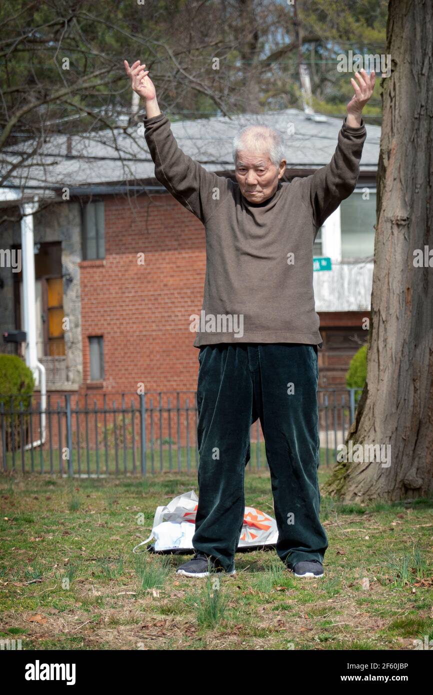 Ein asiatischer Amerikaner, der wahrscheinlich in den Achtzigern ist, führt eine kleine Gruppe in Tai Chi-Bewegungsübungen in einem Park in Queens, New York City.Vertical, Stockfoto