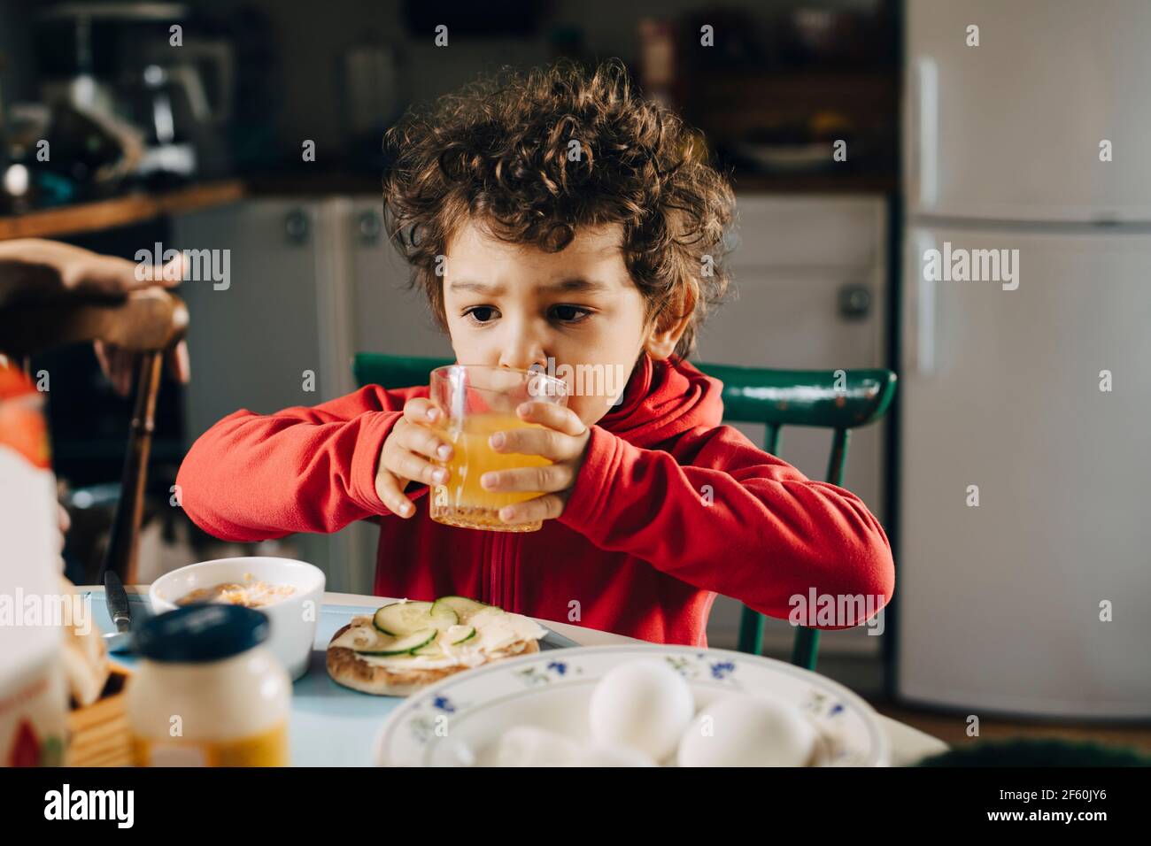 Netter Junge, der beim Frühstück am Tisch Saft trinkt Stockfoto