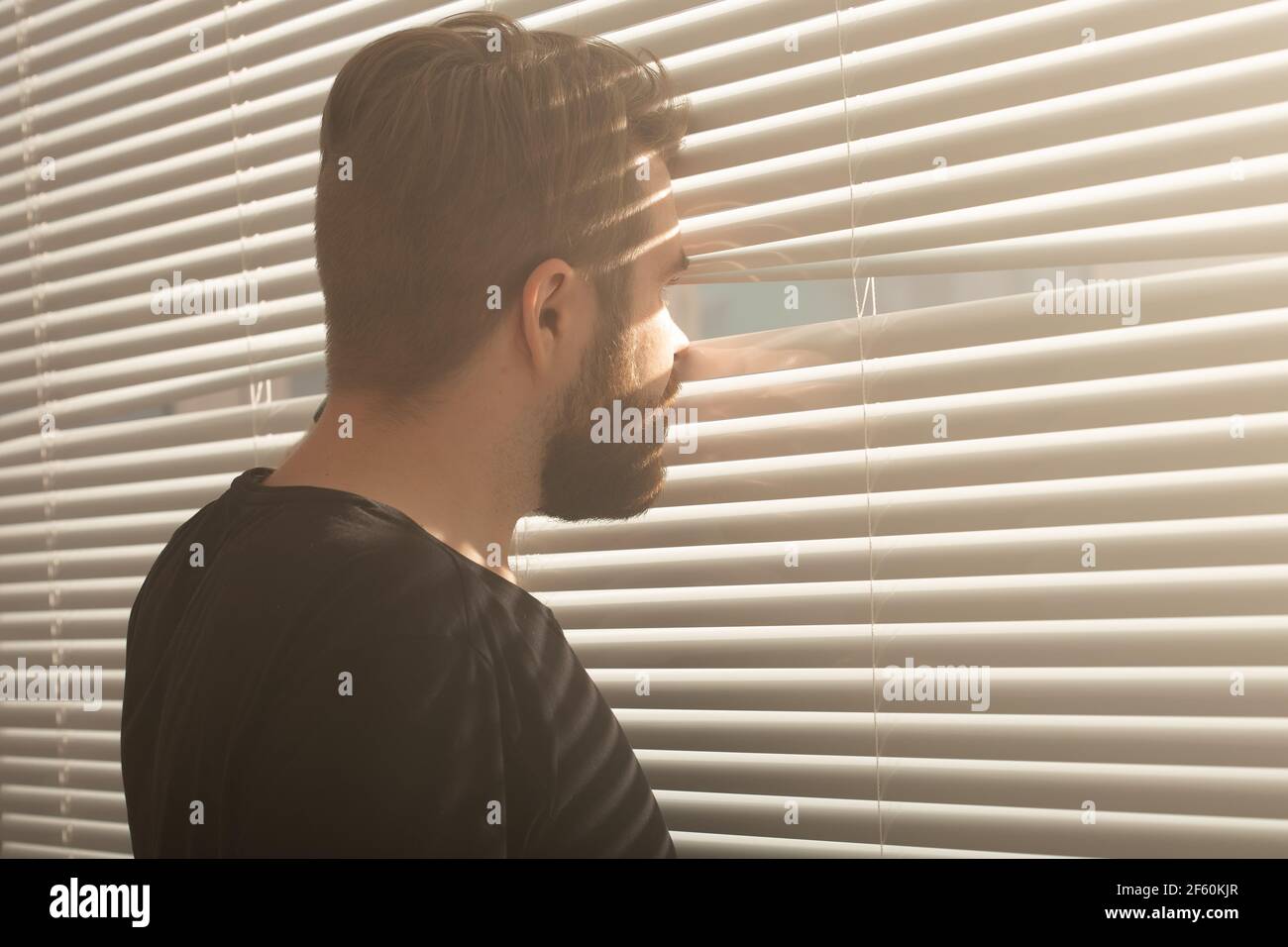 Rückansicht eines jungen Mannes mit Bart, der durch ein Loch in die  Fensterläden blickt und auf die Straße blickt. Überwachung und Neugier  Konzept Stockfotografie - Alamy