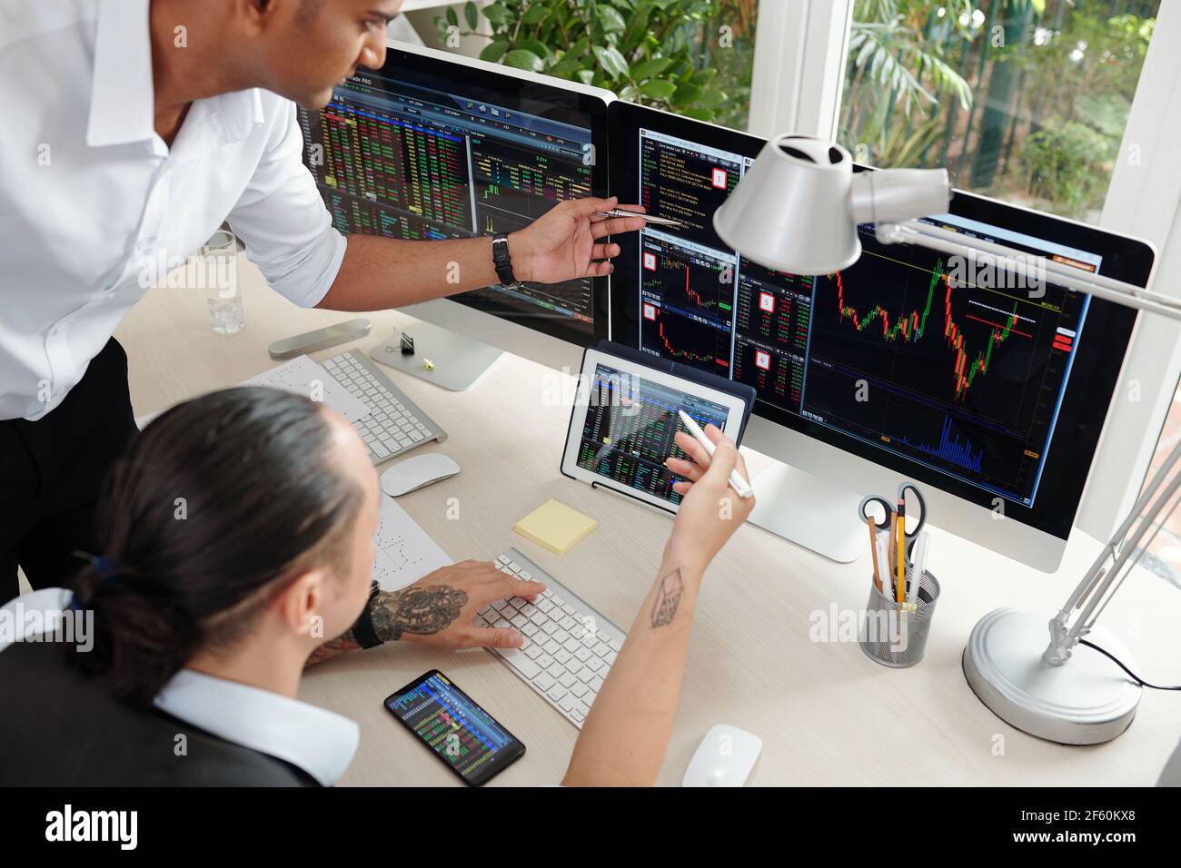 Team von ernsthaften Börsenmaklern, die im Büro mit mehreren Gespräche führen Anzeigen von Bildschirmen und Analysieren von Bestandstrends Stockfoto