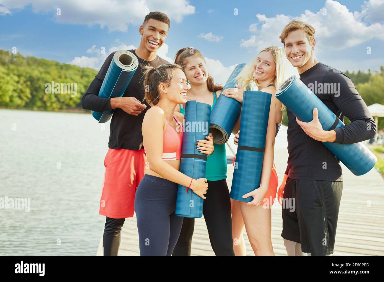 Fröhliche Gruppe von Freunden beim Yoga-Kurs am See Im Sommer mit Yogamatte Stockfoto