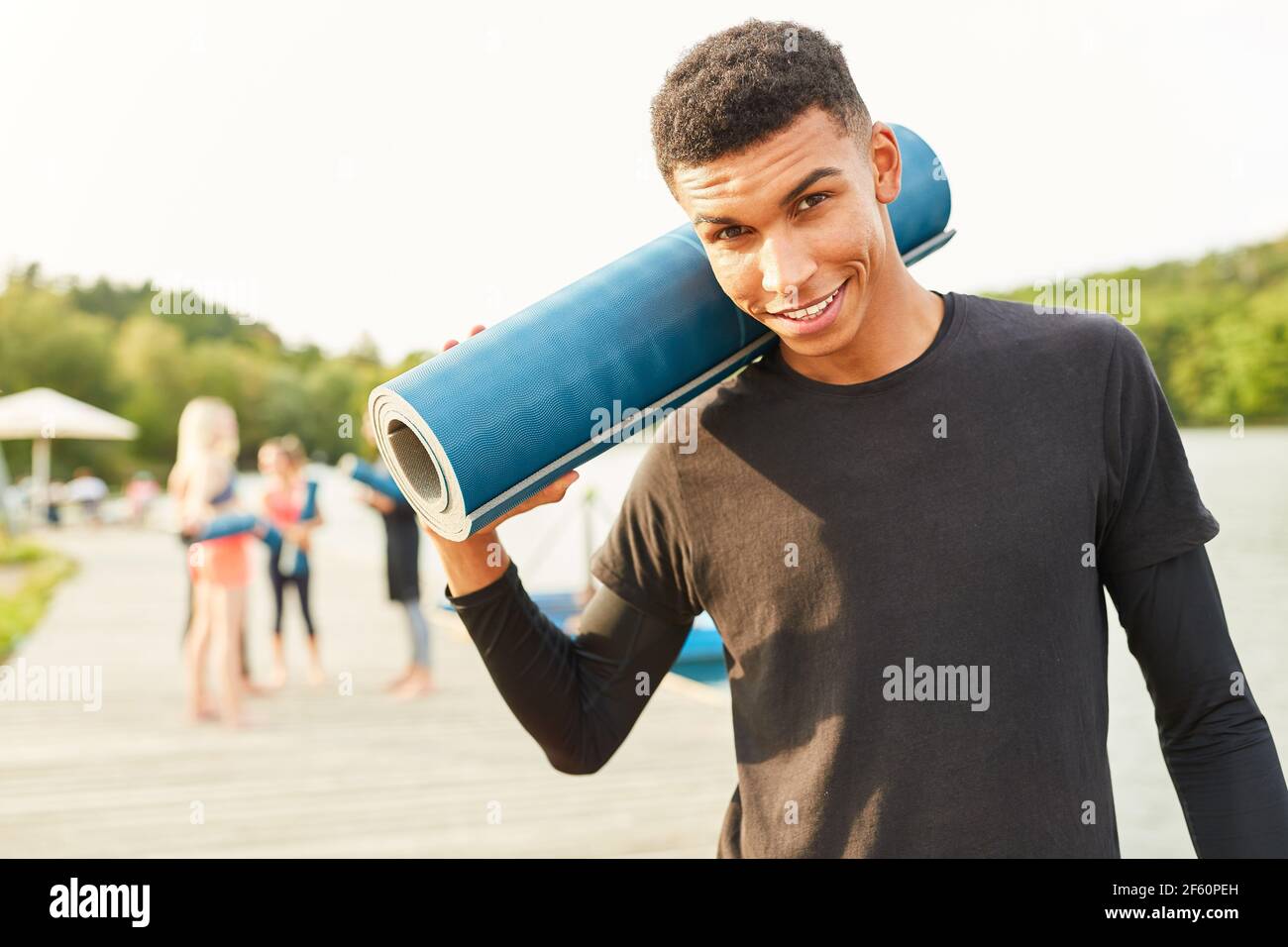 Junger Mann mit Yogamatte als Fitnesstrainer in Natur im Sommer am Seeufer Stockfoto