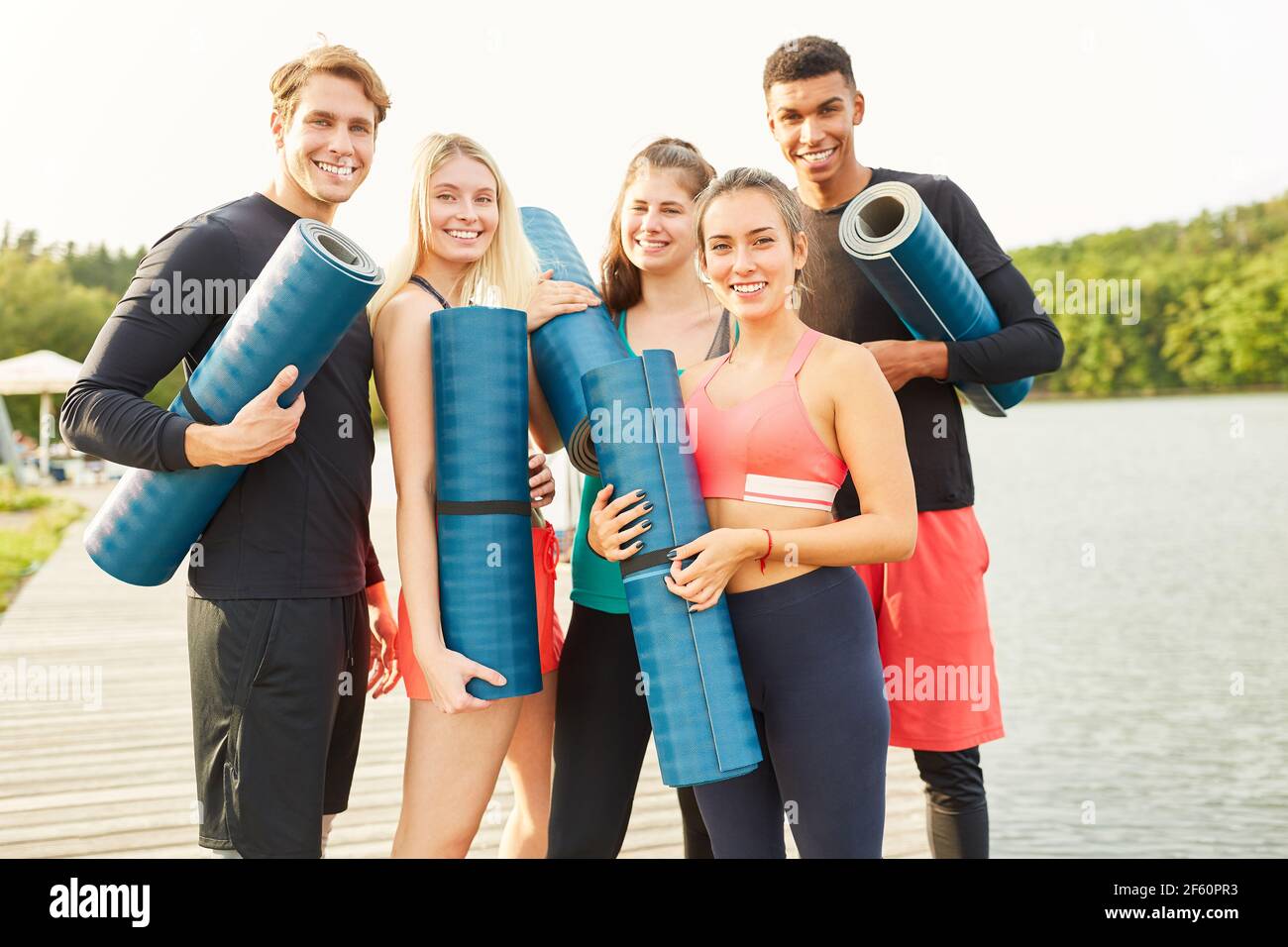 Sportliche Jugendliche mit Yogamatten am Seeufer freuen sich Zu einem Fitnesskurs Stockfoto