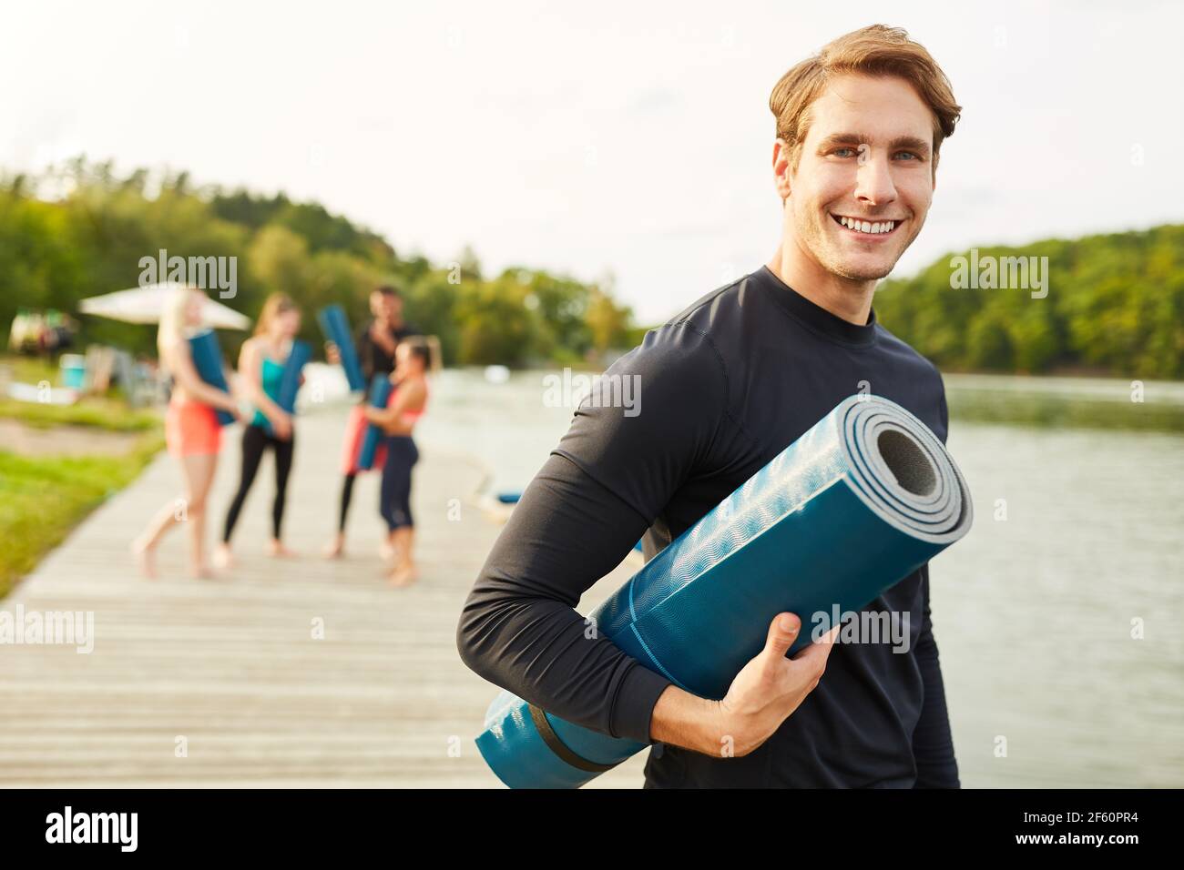 Lächelnder junger Mann als Yogalehrer mit Yogamatte Nach einem Wellnesskurs Stockfoto