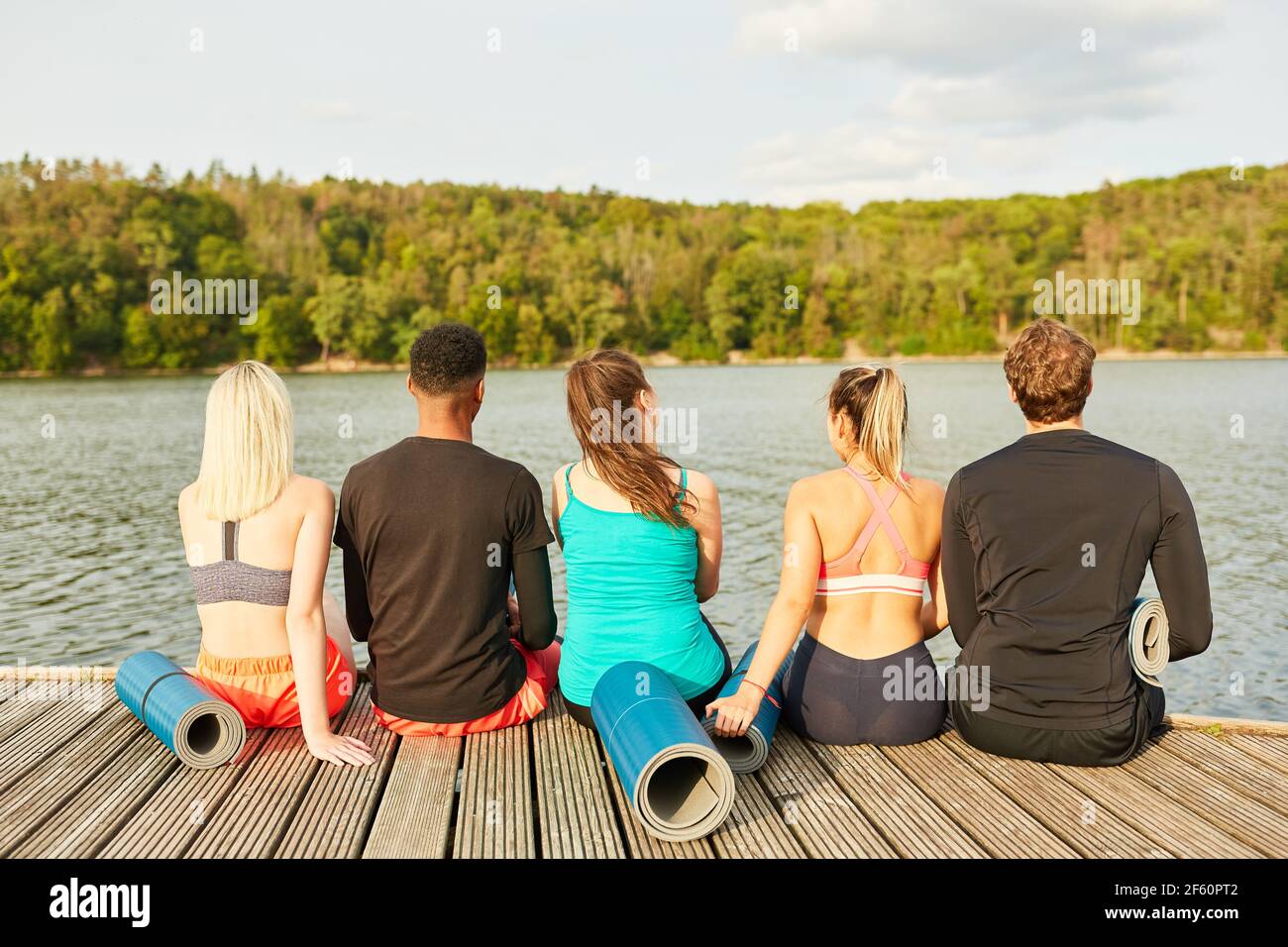 Junge Menschen als Freunde sitzen entspannt in der Natur am see nach einem Fitnesskurs Stockfoto