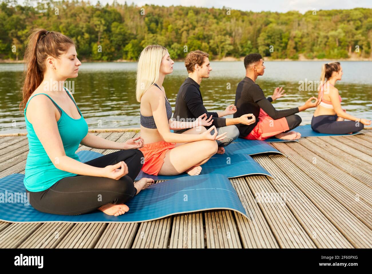 Gruppe von jungen Leuten, die Yoga in einem Wellness-Kurs machen In der Natur am Seeufer Stockfoto