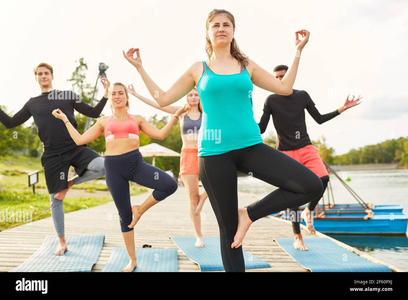 Freunde stehen auf einem Bein und machen Gleichgewichtsübungen im Wellness Yoga-Kurs am See Stockfoto
