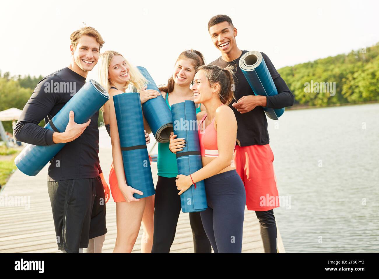 Gruppe von Freunden mit Yoga-Matte lachen glücklich nach einem Fitnesskurs am See Stockfoto