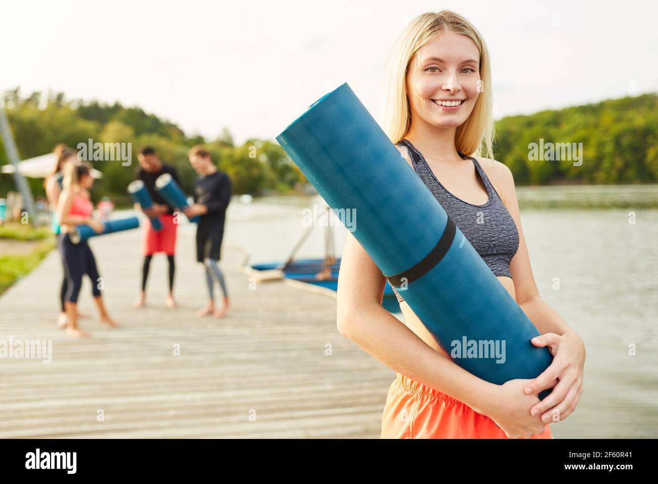 Lächelnde junge Frau mit Yoga-Matte nach einer Fitness oder Yoga-Kurs in der Natur Stockfoto