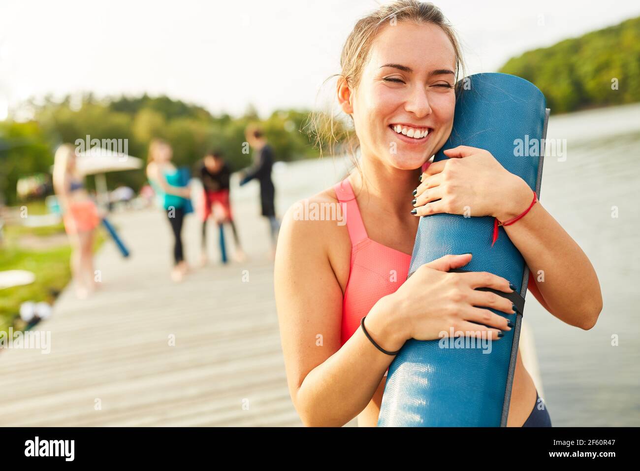 Glückliche junge Frau mit Yogamatte nach dem Fitnesskurs in Natur am See Stockfoto