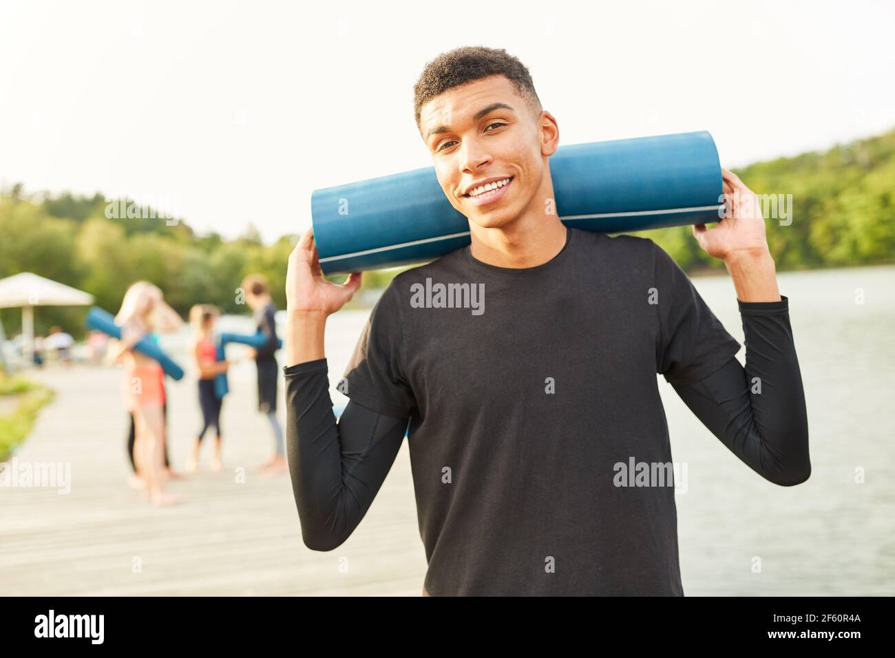 Junger Mann als Yogalehrer oder Fitnesstrainer mit Yoga Matte in der Natur am See Stockfoto