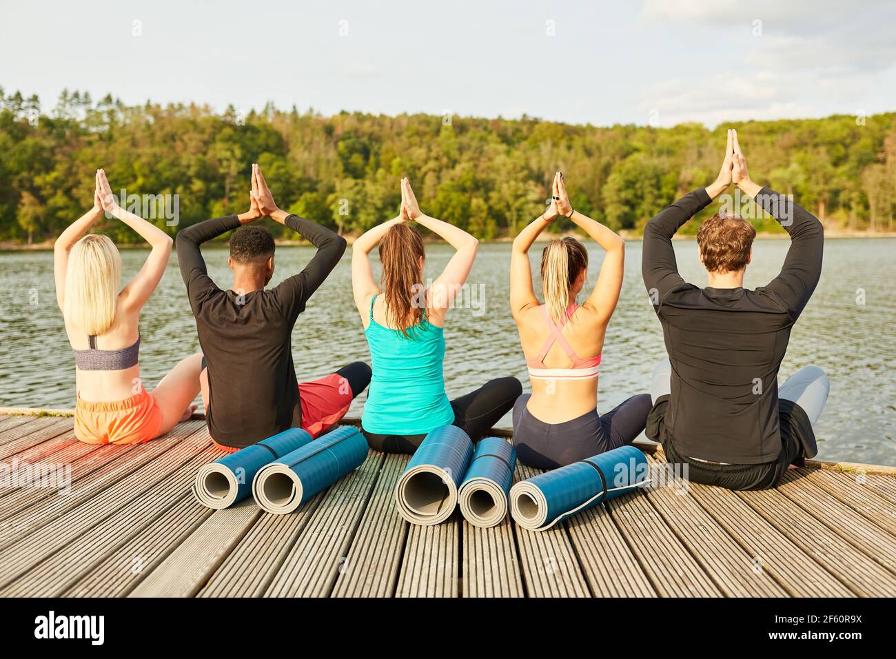 Freunde sitzen in der Natur am Seeufer und tun Eine gemeinsame Yoga-Übung Stockfoto