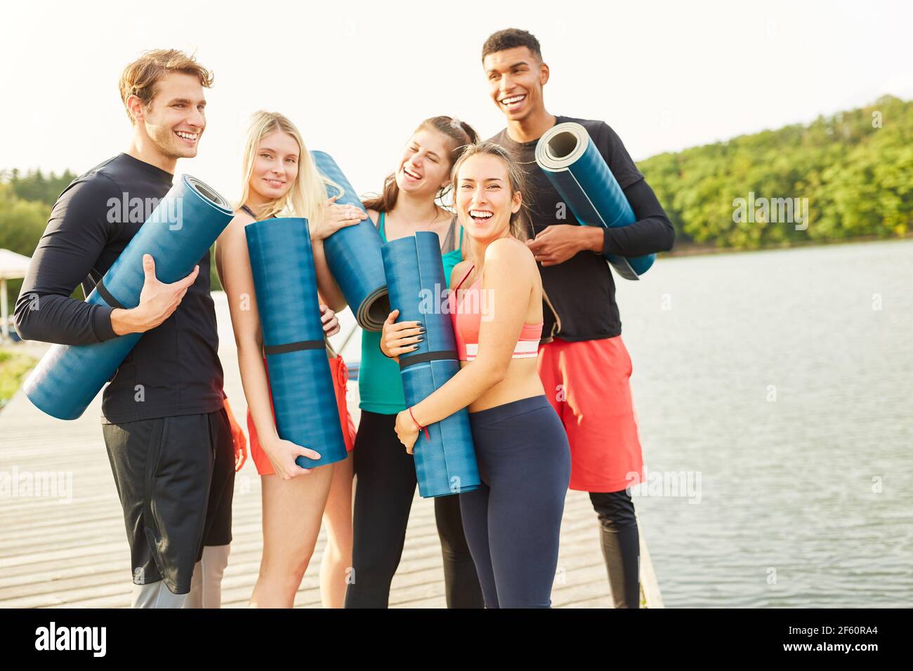 Fröhliche Gruppe von Freunden mit Yoga-Matten in der Natur in Sommer am See Stockfoto