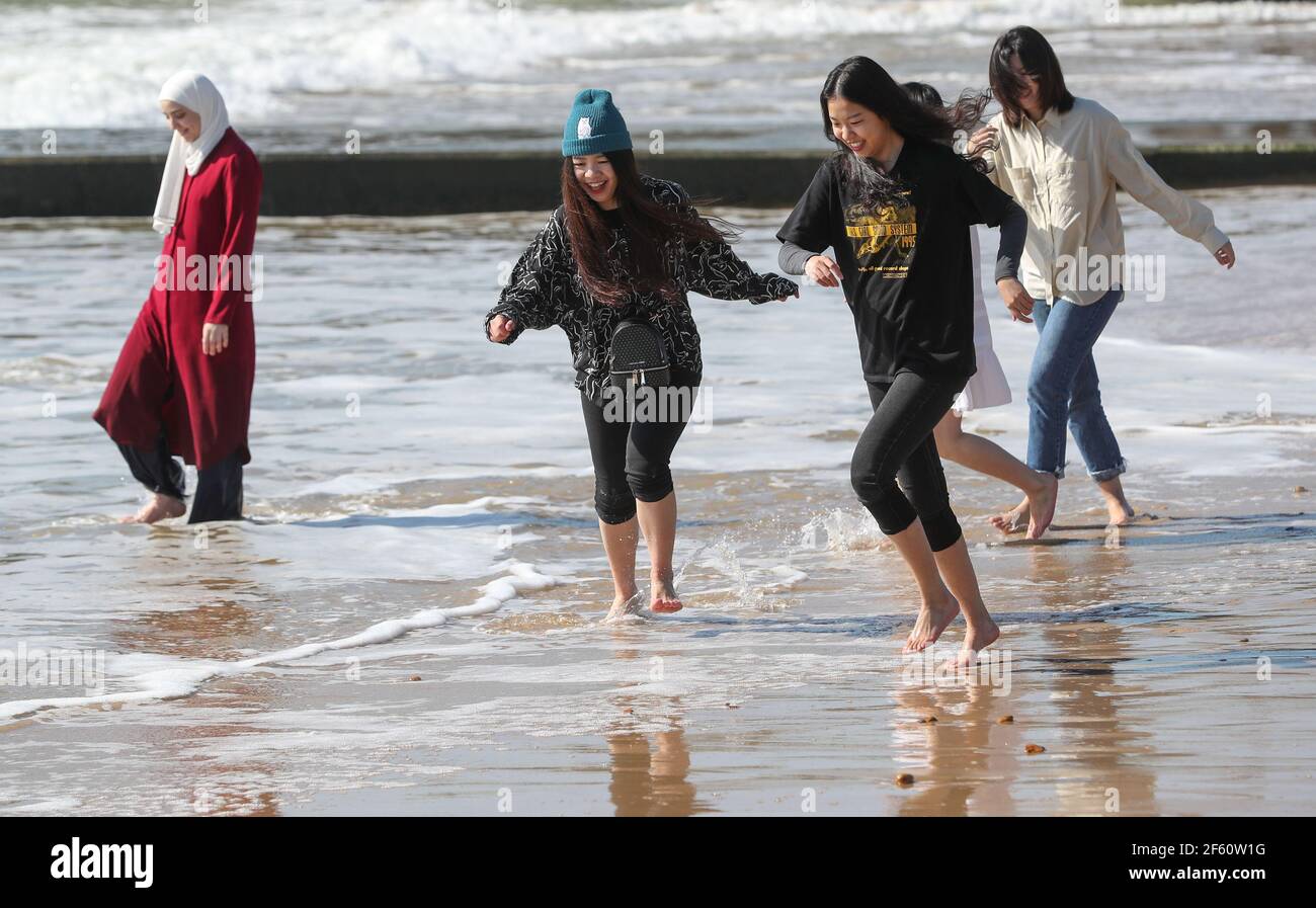 Bournemouth, Großbritannien. 29th. März 2021. Eine Gruppe chinesischer Studenten aus Birmingham hat Spaß in der hellen warmen Märzsonne, um Bournemouth Beach für den Tag am ersten Tag der Lockerung der Covid-19 dritten nationalen Sperrbeschränkungen besuchen, so dass Gruppen von bis zu sechs Freunden in einem Außenbereich zu versammeln. Kredit: Richard Crease/Alamy Live Nachrichten Stockfoto