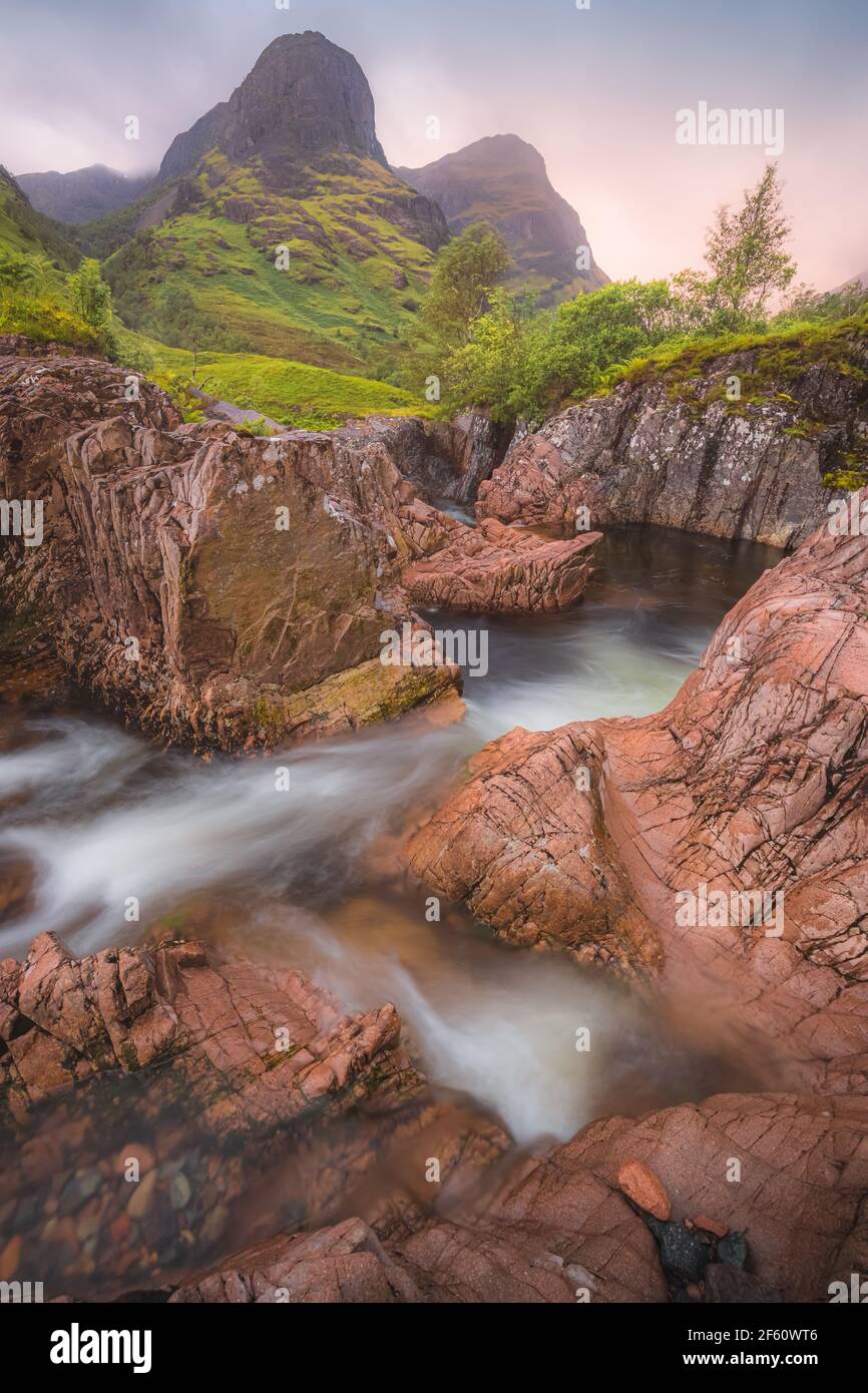 Idyllische Berglandschaft entlang des Flusses Coe zu den Three Sisters of Glencoe mit einem bunten Sonnenuntergang oder Sonnenaufgang in den schottischen Highlands, Schottland. Stockfoto