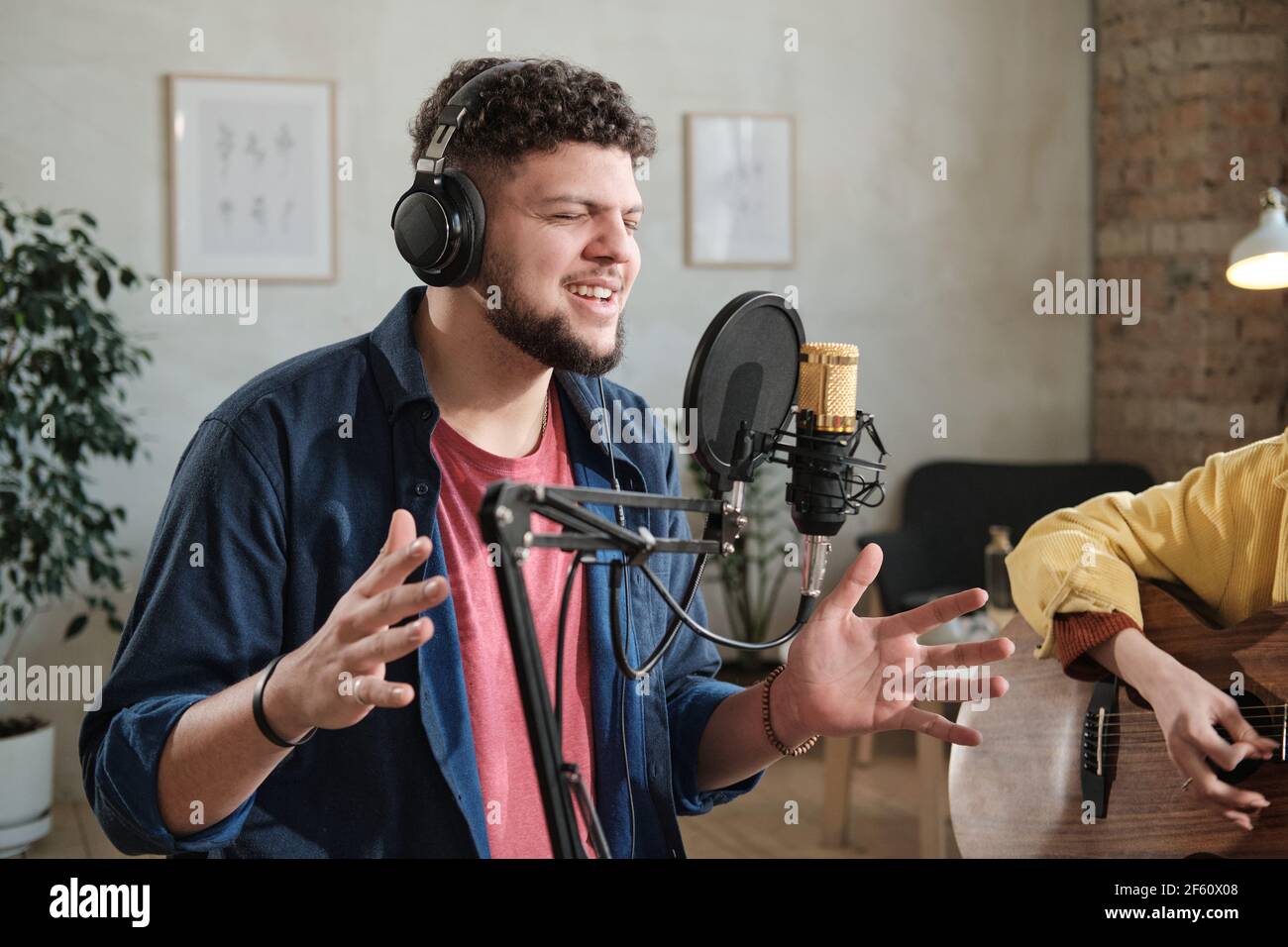 Junge männliche Sängerin in Kopfhörern singen ein Lied in Mikrofon Im Aufnahmestudio Stockfoto