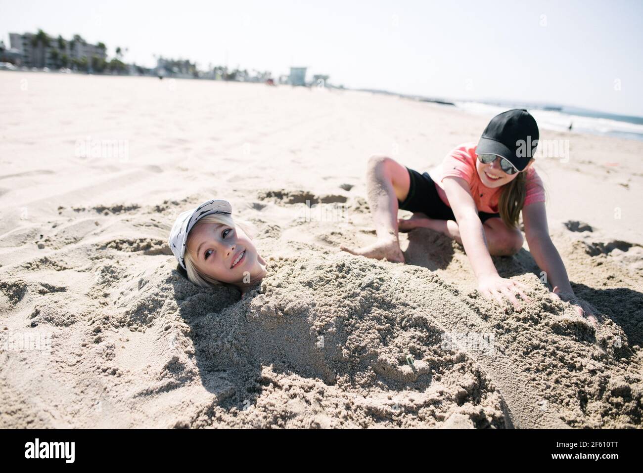 Mädchen begrub Bruder im Sand am Strand Stockfoto