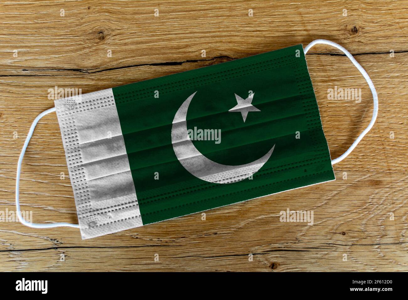 Eine chirurgische Gesichtsmaske mit der bemalten Flagge Pakistans auf einem hölzernen Hintergrund. Konzept von Pakistan während einer Pandemie, Covid-19, Coronavirus. Stockfoto