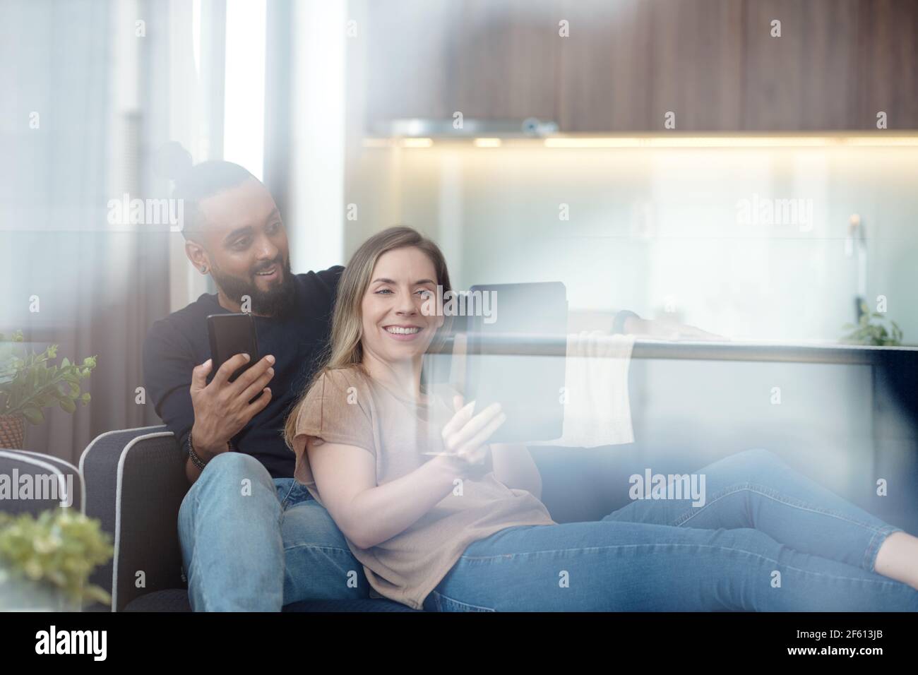 Ziemlich lächelnde junge Frau zeigt etwas Interessantes, das sie auf gefunden internet für Ehemann, wenn sie sich auf dem Sofa ausruhen Zu Hause Stockfoto