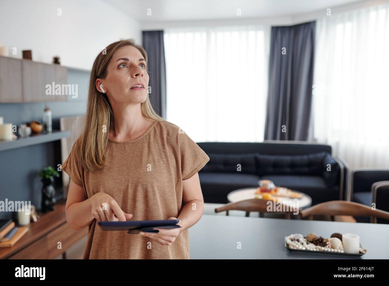 Hübsche Frau mit digitalen Tablet mit Smart-Home-Anwendung Steuern Sie Temperatur und Licht in ihrer Wohnung Stockfoto