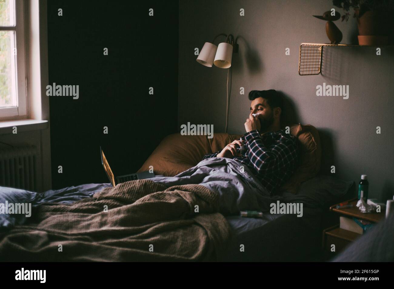 Kranker Mann bläst die Nase, während er Online-Beratung auf dem Laptop hat Zu Hause Stockfoto