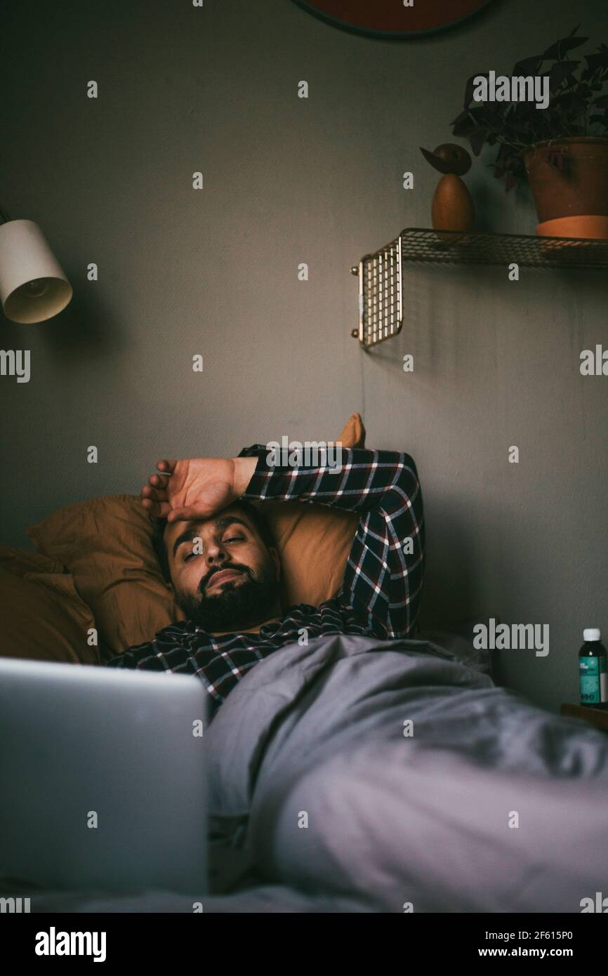 Kranker Mann mit Online-Beratung auf dem Laptop, während er auf lag Bett Stockfoto