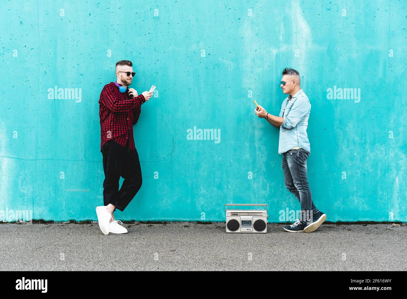 Paar Männer mit Handy vor einer blauen Wand Hintergrund - Konzept der Verliebtheit mit Technologie, soziale Netzwerke und Handy - LGBT Stockfoto