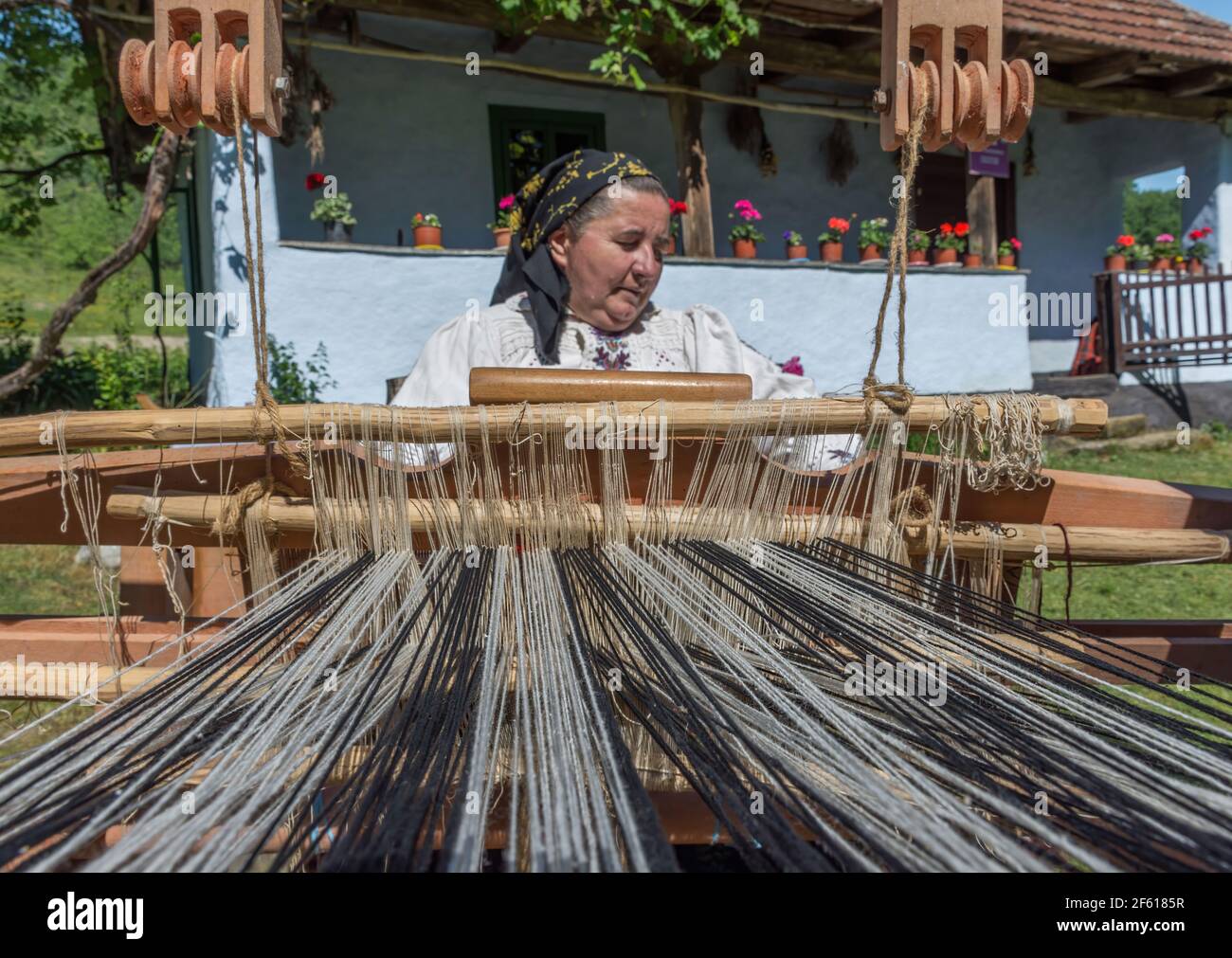 Salaj, Transsilvanien, Rumänien-14. Mai 2018: Alte Frau in traditioneller rumänischer Volkstracht, die an der alten Holzwebmaschine vor ihrem Saibling arbeitet Stockfoto
