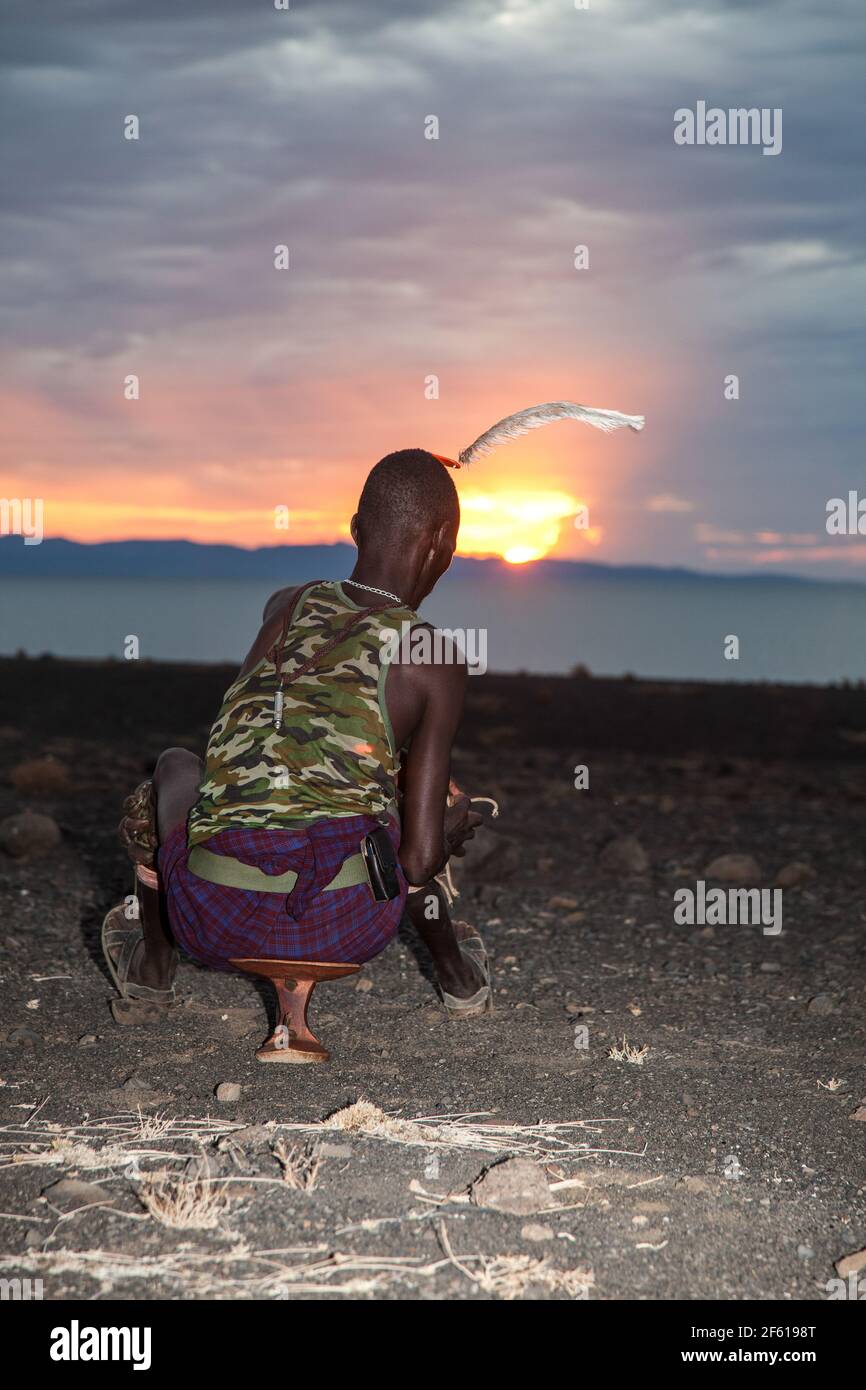 Turkana Mann sitzt in einem traditionellen Stuhl bei Sonnenuntergang. Turkana ist ein nilotisches Volk, das im Kreis Turkana im Nordwesten Kenias beheimatet ist Stockfoto