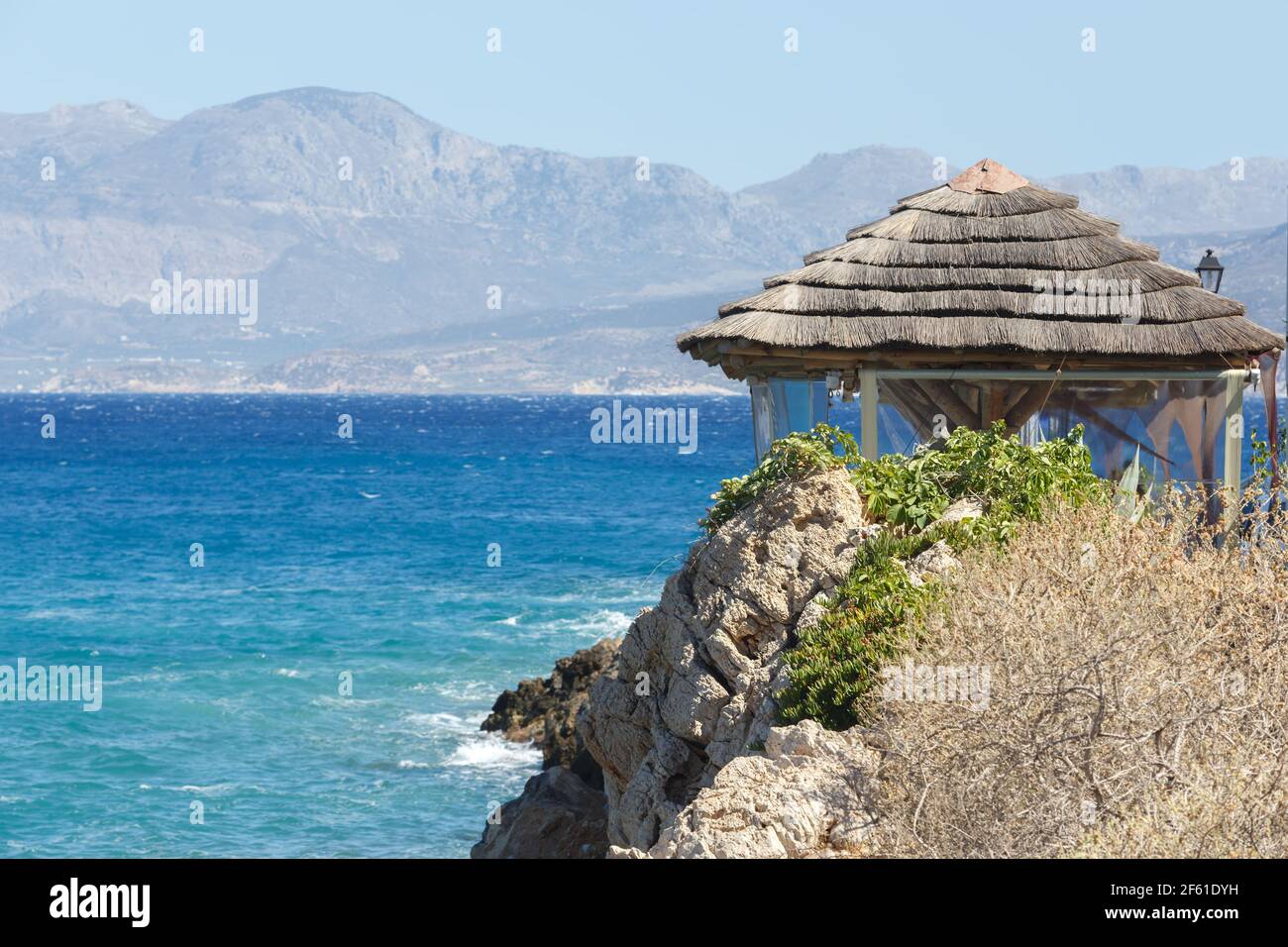Pavillon mit Strohdach auf einem felsigen Strand gegenüber Hintergrund der Berge Stockfoto