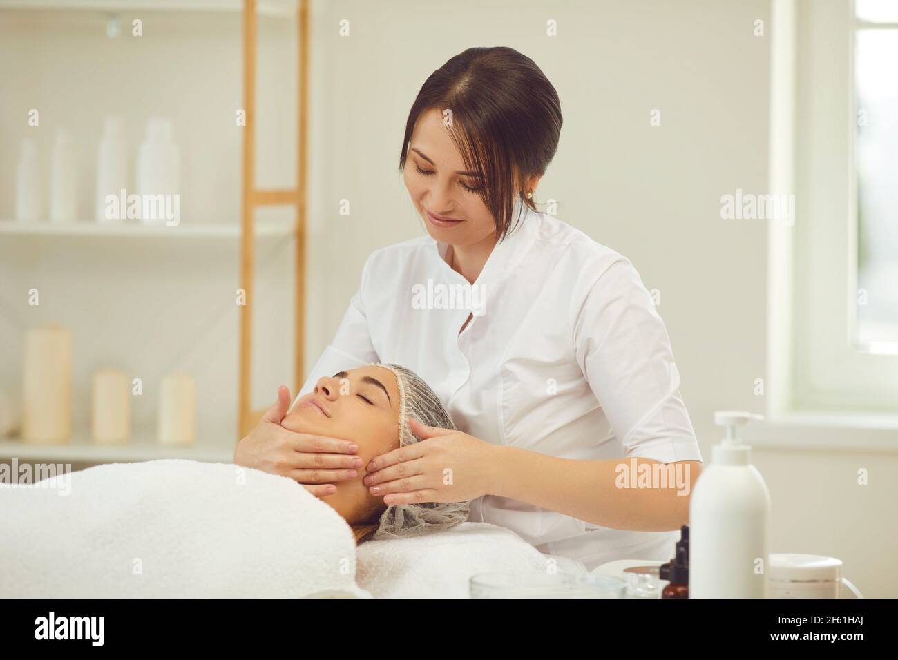 Lächelnde Frau Dermatologe macht manuelle entspannende Gesichtsmassage für Frau Stockfoto