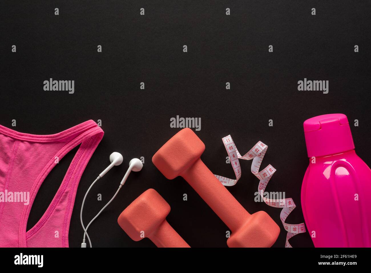 Kurzhanteln, Maßband, Wasserflasche, Kopfhörer und Sportbekleidung auf schwarzem Hintergrund. Fitness-, Sport- und Trainingskonzept Flat Lay mit Kopierfläche. Stockfoto