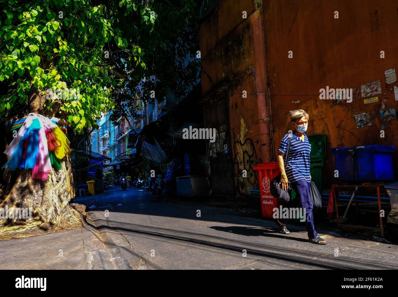 Ein Mann geht entlang einer sonnendurchfluteten Gasse in Talat Noi, Bangkok, Thailand Stockfoto