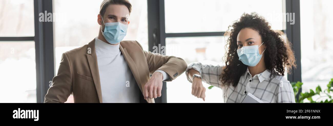 Multikulturelle Geschäftsleute in medizinischen Masken tun Ellenbogen Beule im Büro, Banner Stockfoto