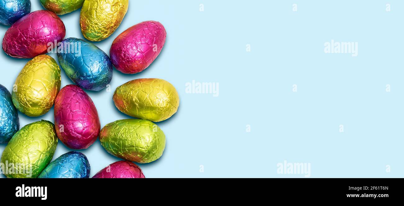 Seitenrand von bunt gewickelten Schokolade Ostereier auf blauem Hintergrund. Draufsicht. Stockfoto