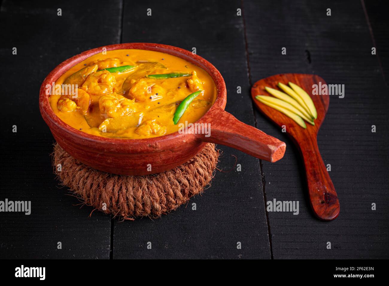 Garnelen Mango Curry, kerala traditionelle Gericht mit roher Mango und Angeordnet in einer irdenen Ware mit schwarzem texturierten Hintergrund Stockfoto