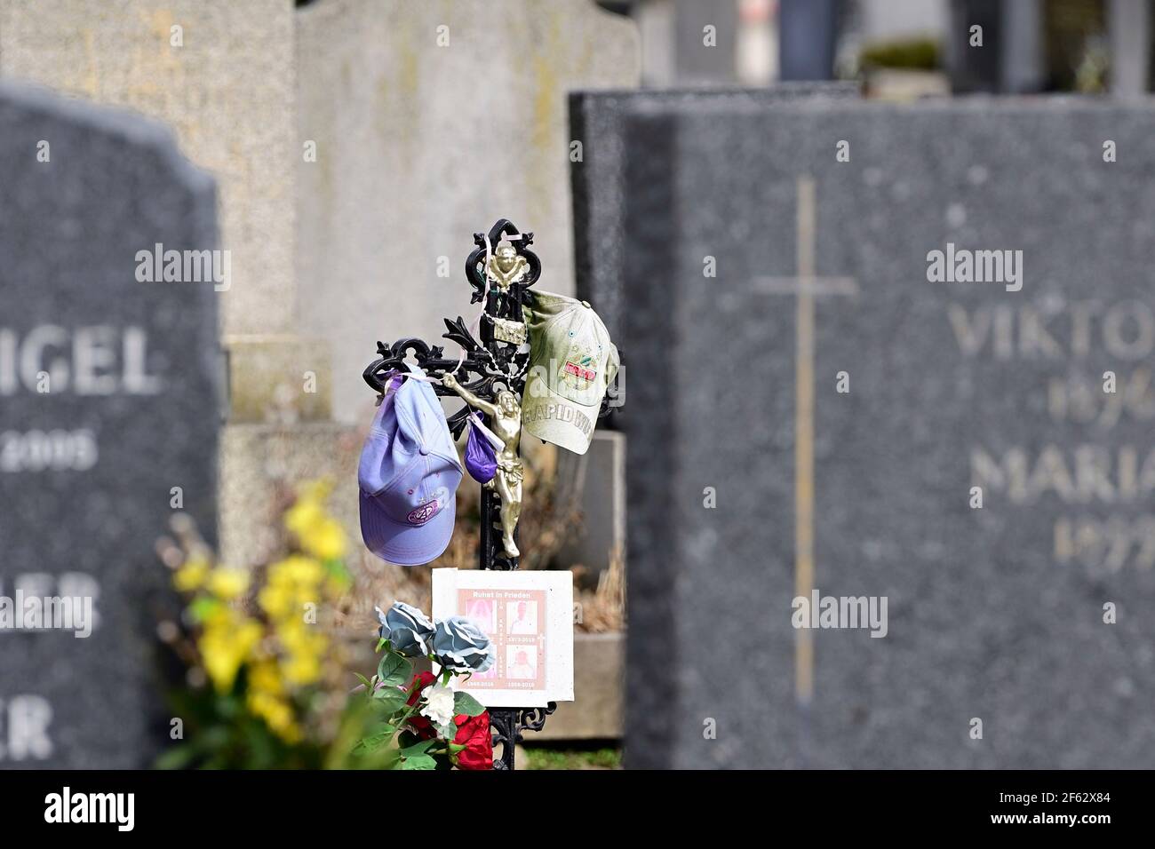 Wien, Österreich. Der zentrale Friedhof in Wien. Zwei Baseballkappen der Fußballvereine Austria Wien und Rapid Wien auf einem Grabkreuz Stockfoto